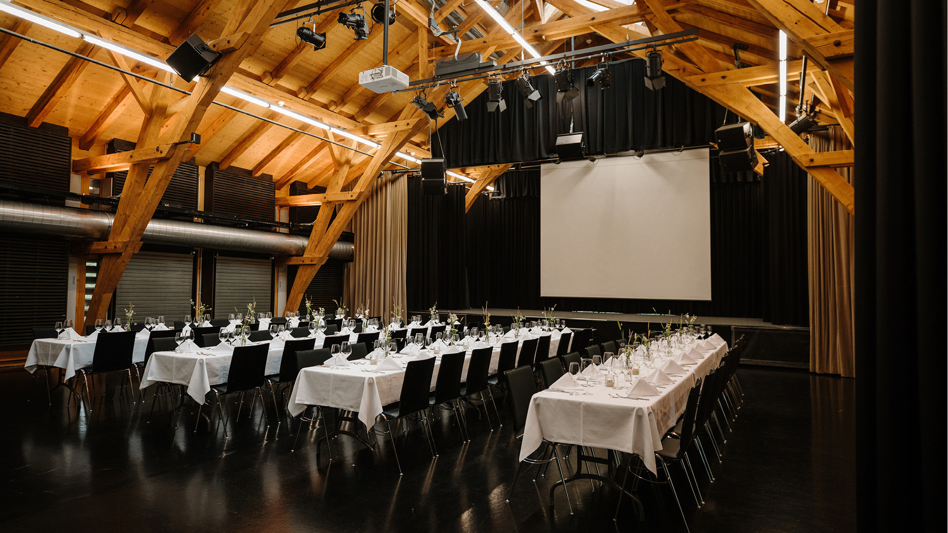 The upper floor of the Schüür event venue with four long rows of tables set for dinner.