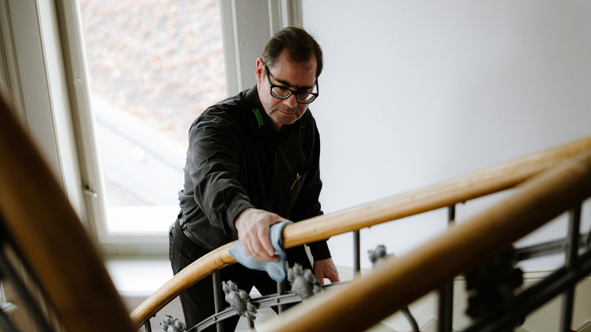 Une personne en chemise noire qui nettoie la rampe d'escalier avec un chiffon bleu.